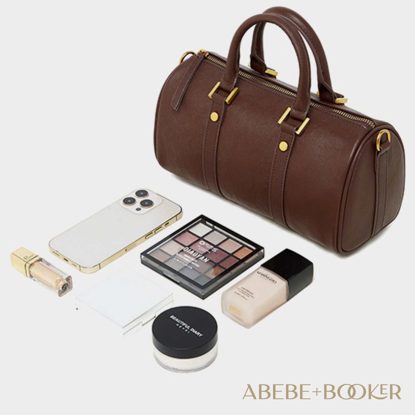 Classic leather barrel handbag with gold hardware, surrounded by daily essentials.