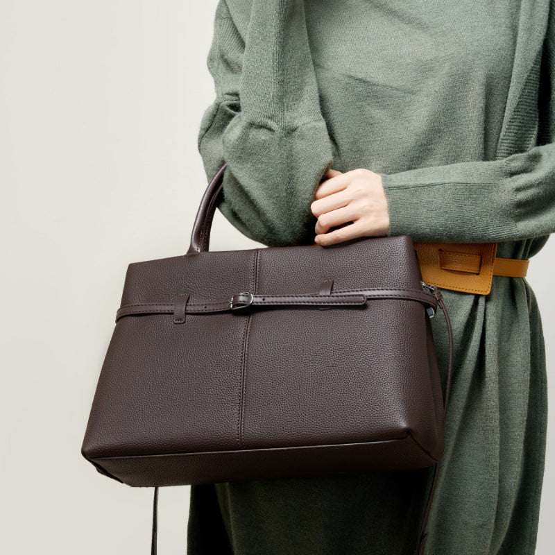 Women's leather briefcase bag in brown, held by a model in a green outfit, showcasing