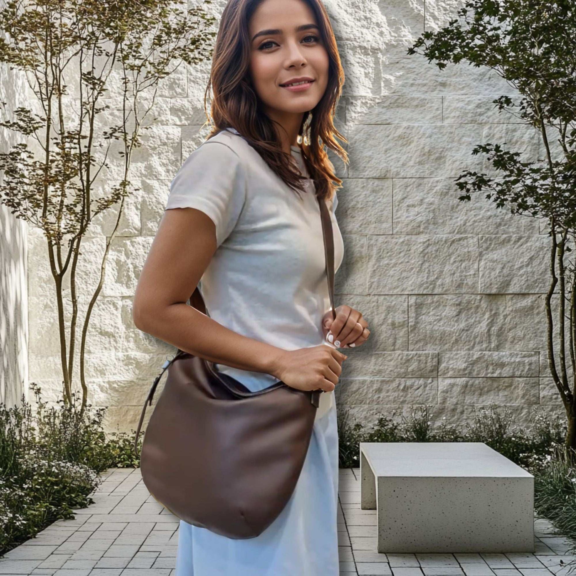 Woman holding a brown leather slouchy crossbody bag outdoors.