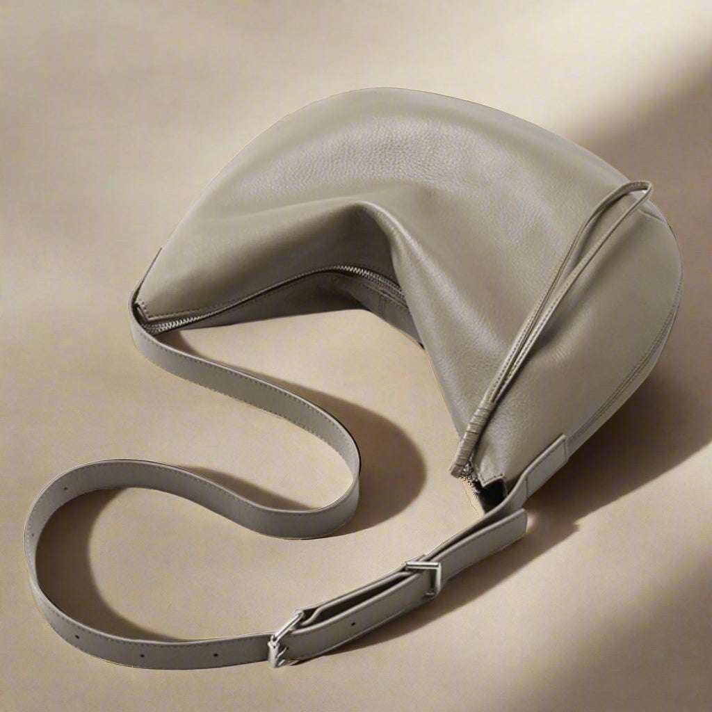 Slouchy crossbody bag in genuine leather with adjustable strap on beige surface.