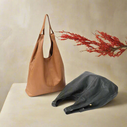 Slouchy leather hobo bags in tan and black on display surface with red foliage accent.