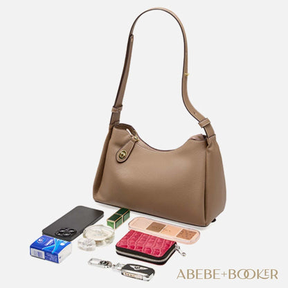 Trapezoid Leather Crossbody Handbag in brown with accessories displayed around it. Scratch-resistant genuine leather