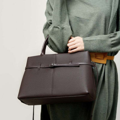 Women's leather briefcase bag in brown, held by a model in a green outfit, showcasing