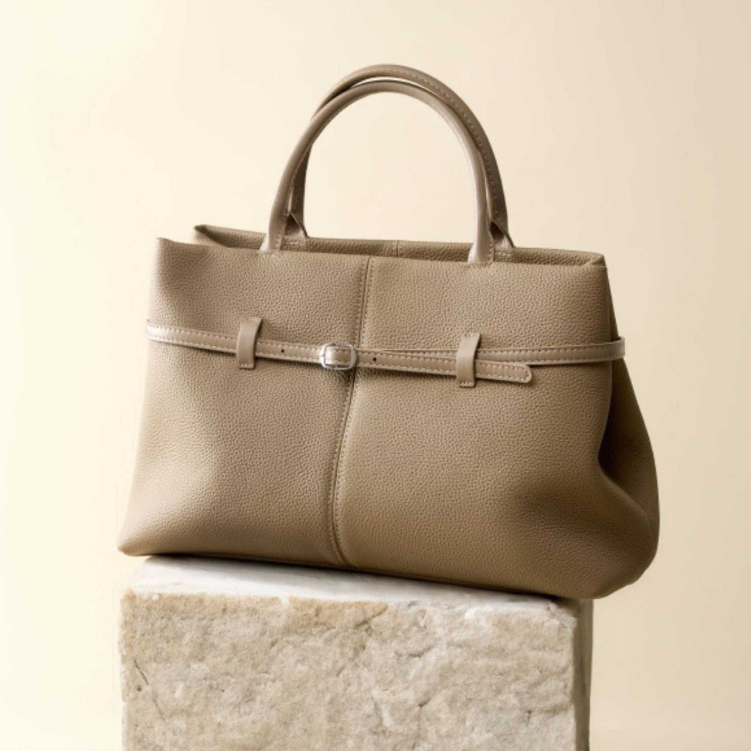 Women's genuine leather briefcase bag with chic buckle detail on a stone pedestal.